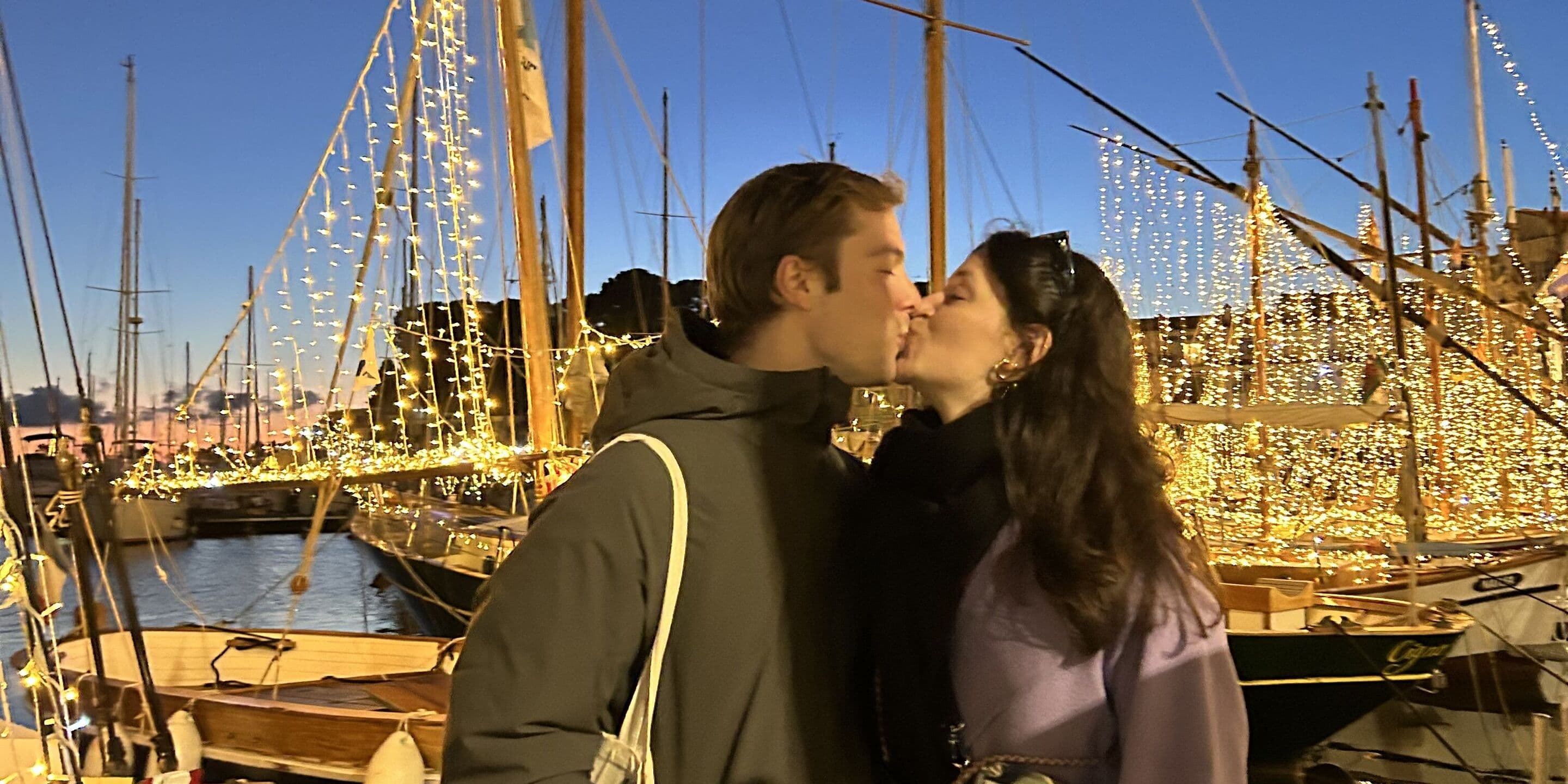 Lucie & Damian kissing in a harbour full of fairy-lit boats